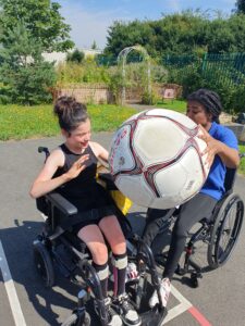 A woman teaching a young girl how to play a wheelchair ball game